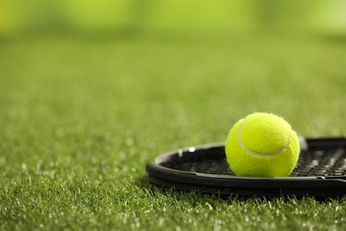 Photo of Tennis racket and ball on green artificial grass, closeup. Space for text