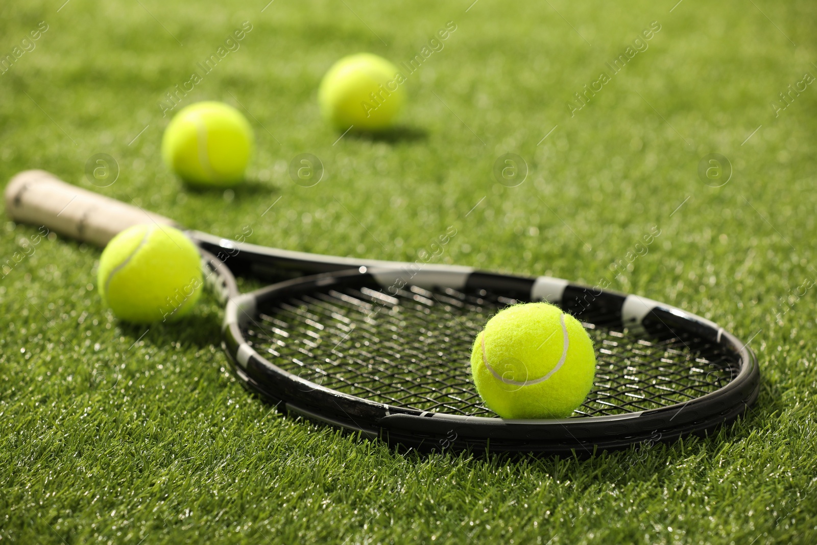 Photo of Tennis racket and balls on green artificial grass, closeup