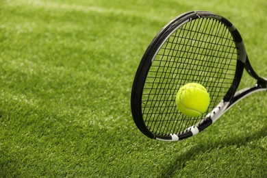 Photo of Tennis racket with ball on green artificial grass, closeup. Space for text