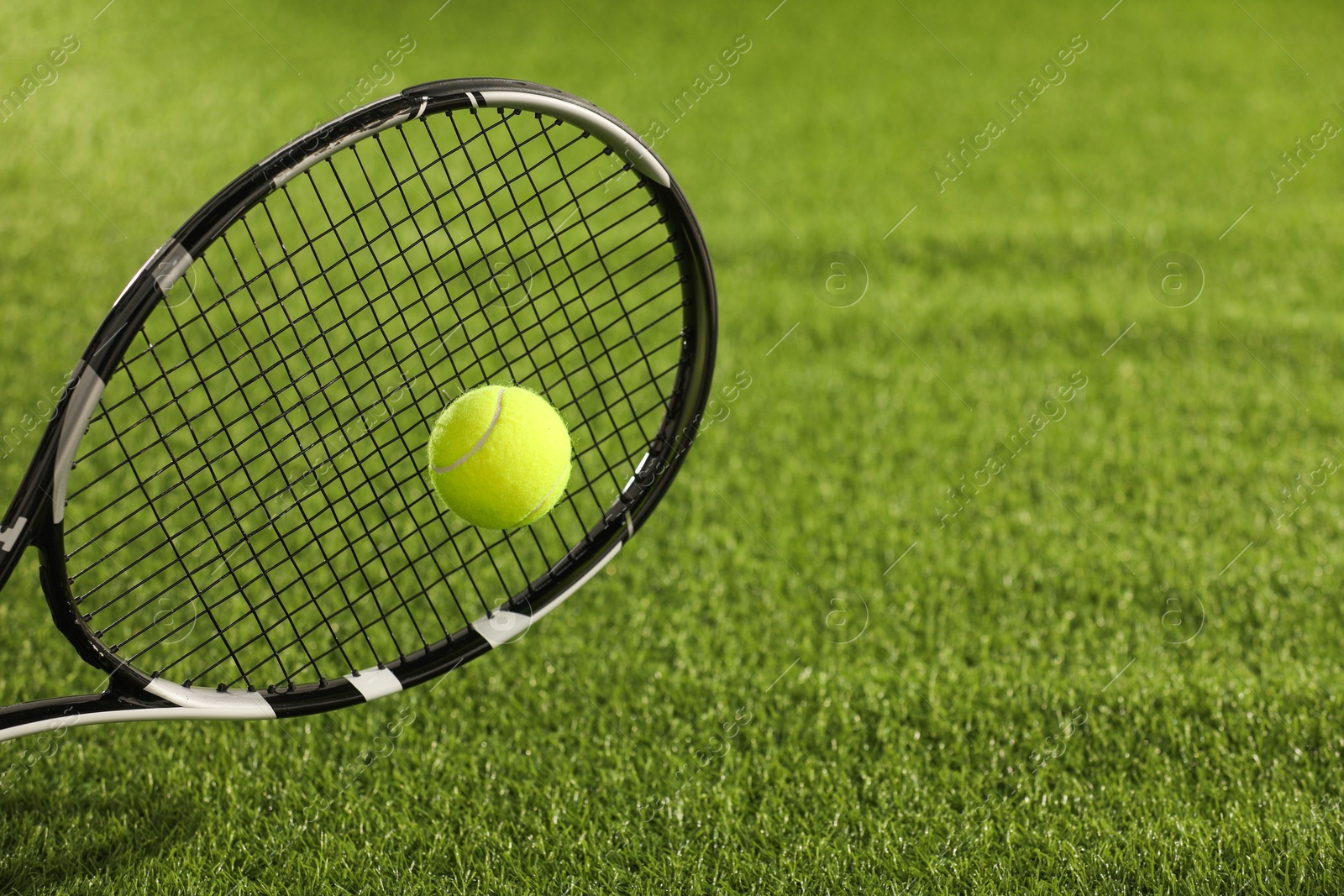 Photo of Tennis racket with ball on green artificial grass, closeup. Space for text