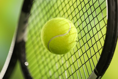 Tennis racket with ball against blurred green background, closeup