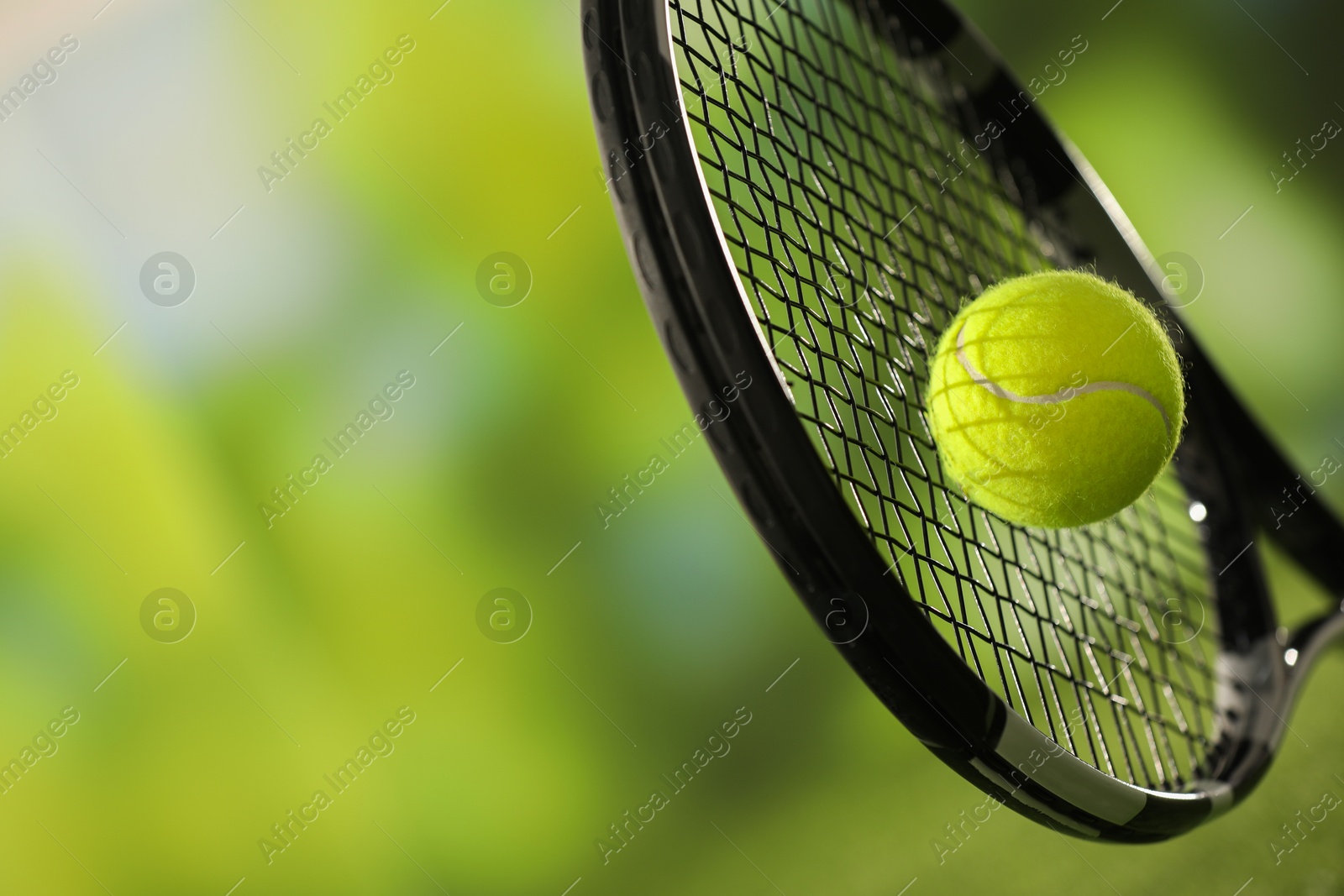 Photo of Tennis racket with ball against blurred green background, closeup. Space for text