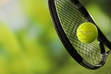 Photo of Tennis racket with ball against blurred green background, closeup. Space for text