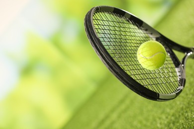 Photo of Tennis racket with ball on green artificial grass, closeup. Space for text