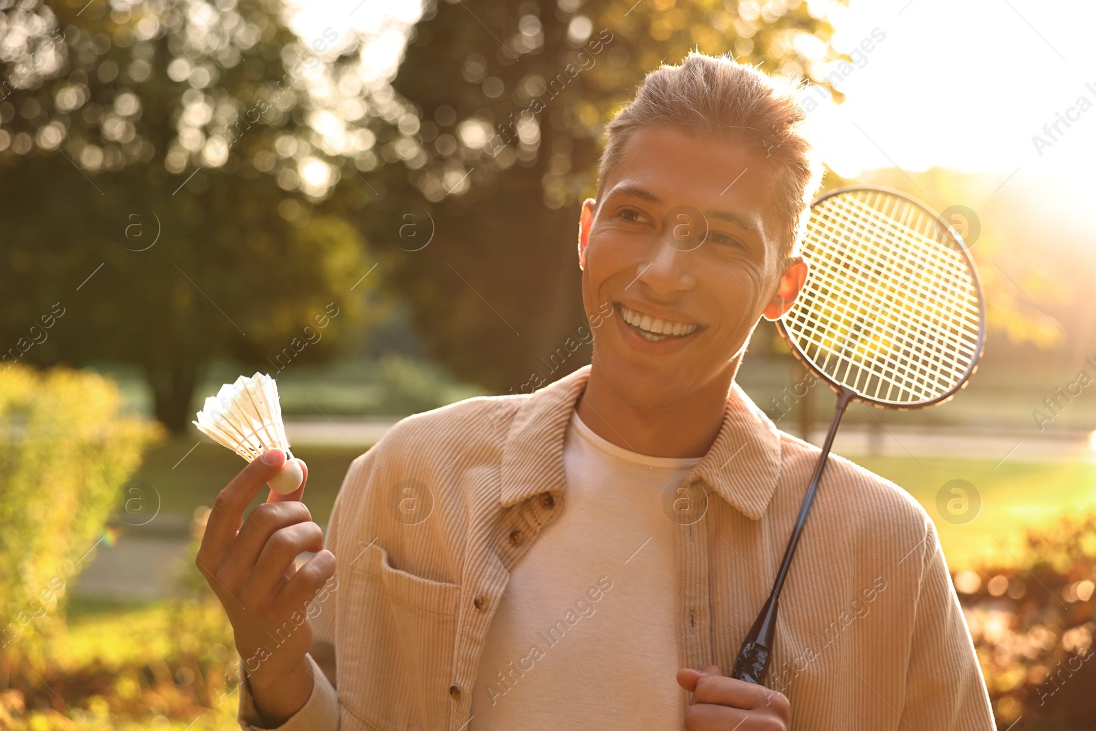 Photo of Happy young man with badminton racket and shuttlecock in park on sunny day