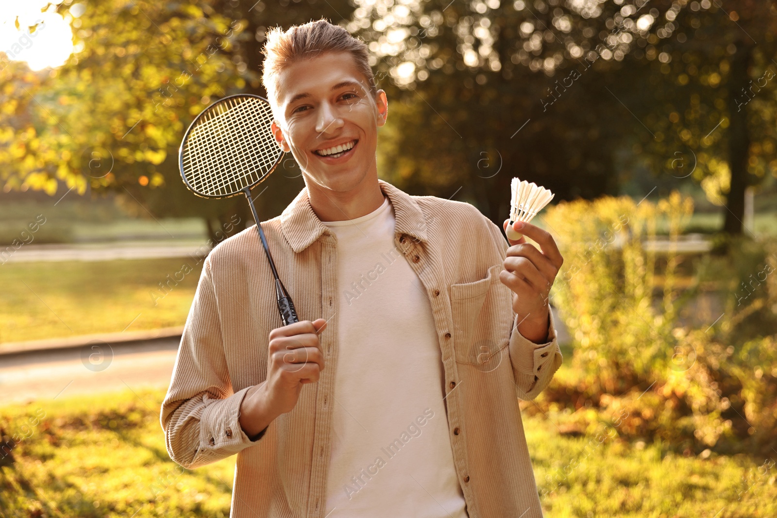 Photo of Happy young man with badminton racket and shuttlecock in park on sunny day