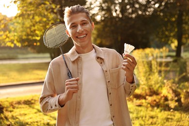 Happy young man with badminton racket and shuttlecock in park on sunny day