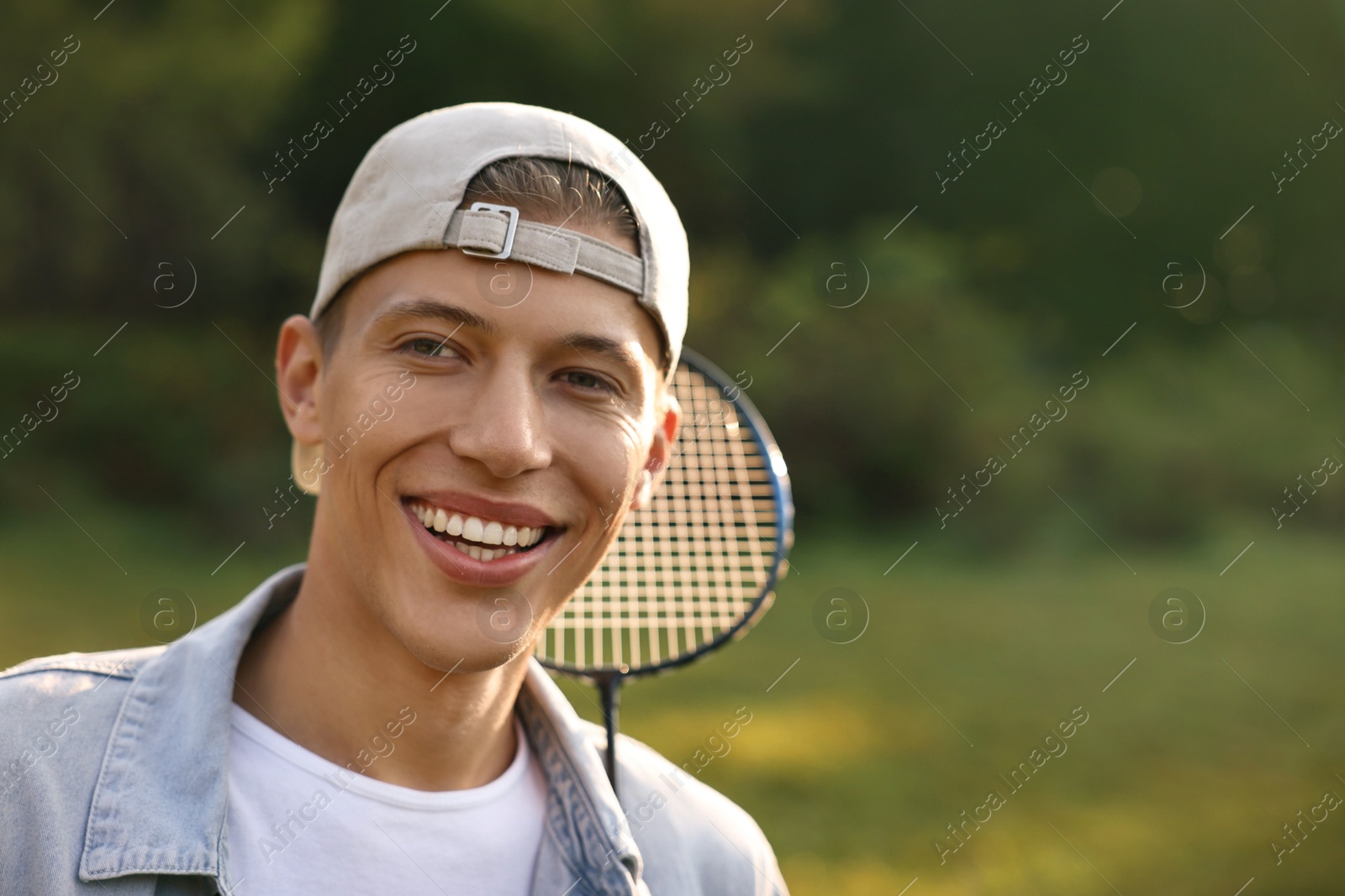 Photo of Happy young man with badminton racquet in park, space for text