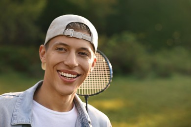 Photo of Happy young man with badminton racquet in park, space for text