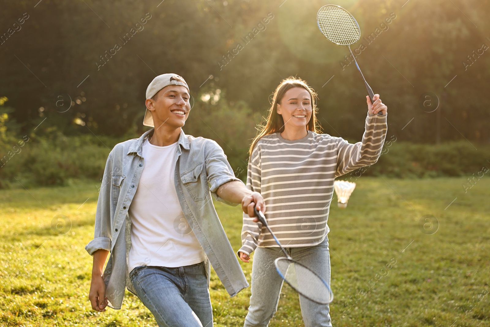 Photo of Young woman and man playing badminton in park on sunny day