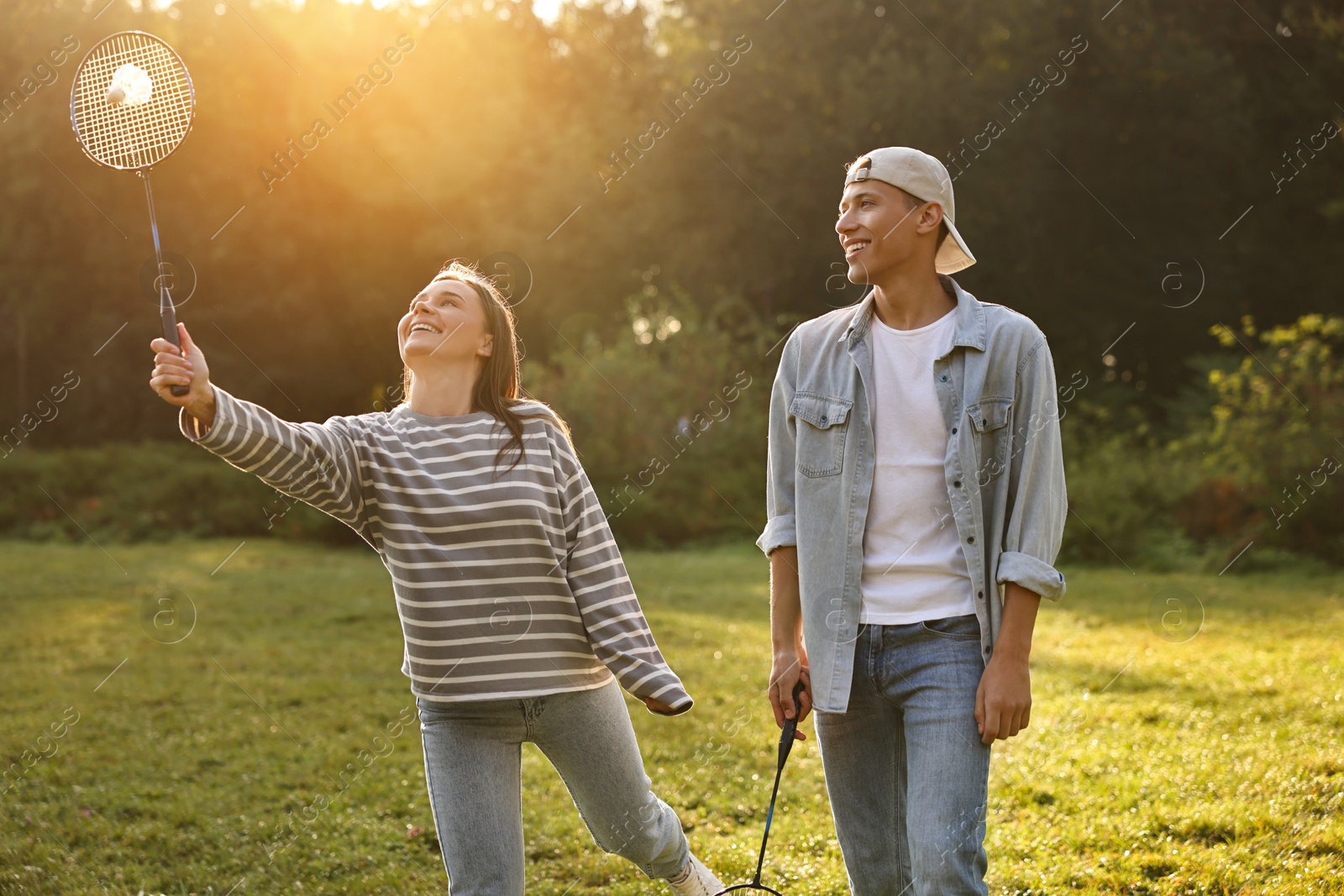 Photo of Young woman and man playing badminton in park on sunny day