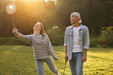 Young woman and man playing badminton in park on sunny day