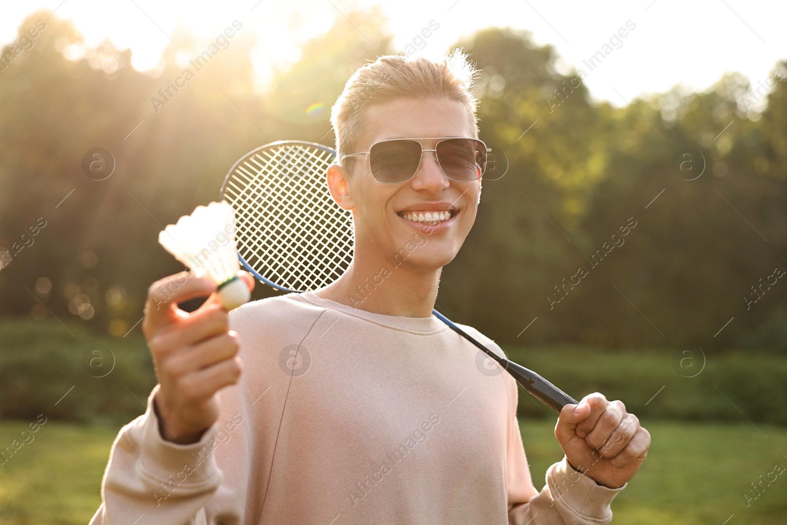 Photo of Happy young man with badminton racket and shuttlecock in park on sunny day