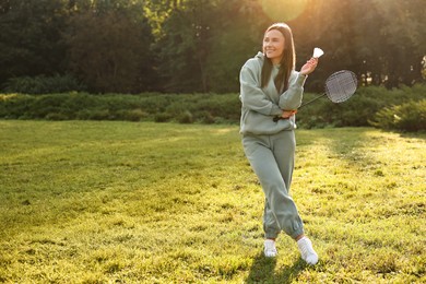 Photo of Happy young woman with badminton racket and shuttlecock in park on sunny day, space for text