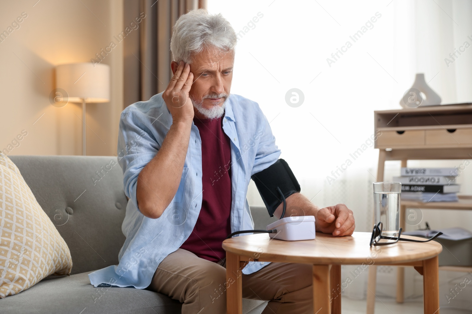 Photo of Senior man measuring blood pressure at table indoors