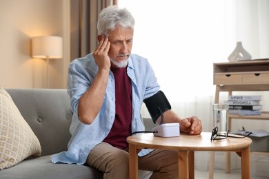 Senior man measuring blood pressure at table indoors