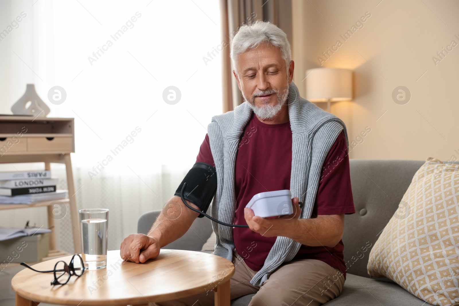 Photo of Senior man measuring blood pressure on sofa indoors