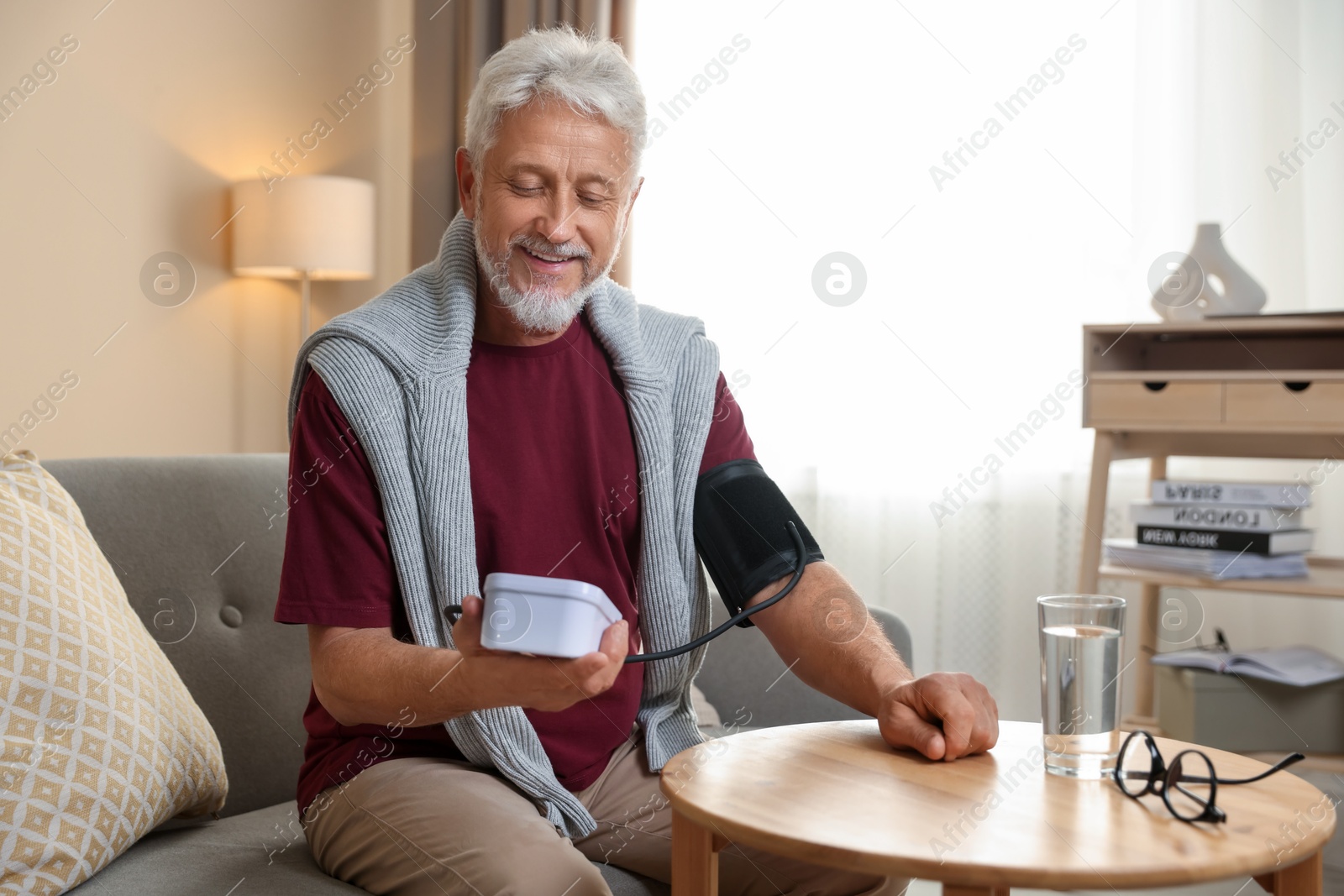 Photo of Senior man measuring blood pressure on sofa indoors