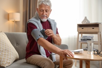 Photo of Senior man measuring blood pressure on sofa indoors