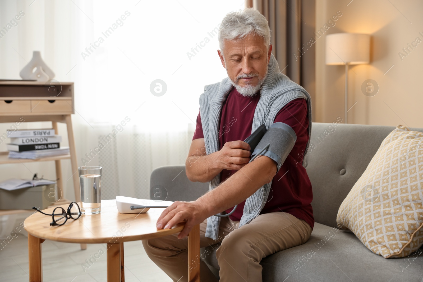 Photo of Senior man measuring blood pressure on sofa indoors