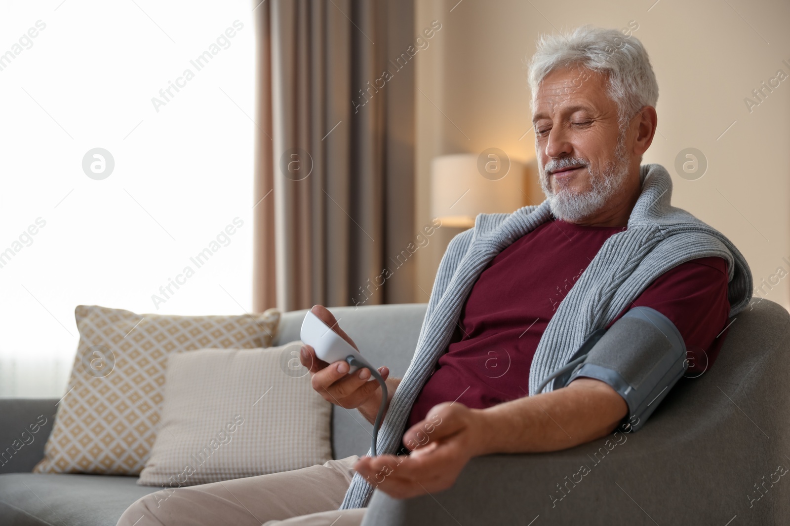 Photo of Senior man measuring blood pressure on sofa indoors