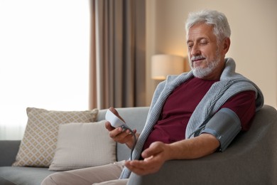 Photo of Senior man measuring blood pressure on sofa indoors