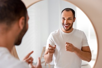 Photo of Smiling man looking at mirror in bathroom