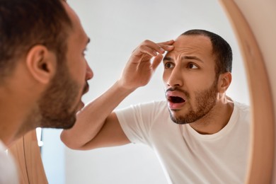 Photo of Worried man looking at mirror in bathroom