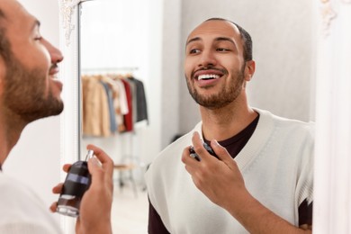 Photo of Smiling man spraying perfume near mirror at home