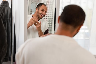 Photo of Smiling man looking at mirror at home, back view