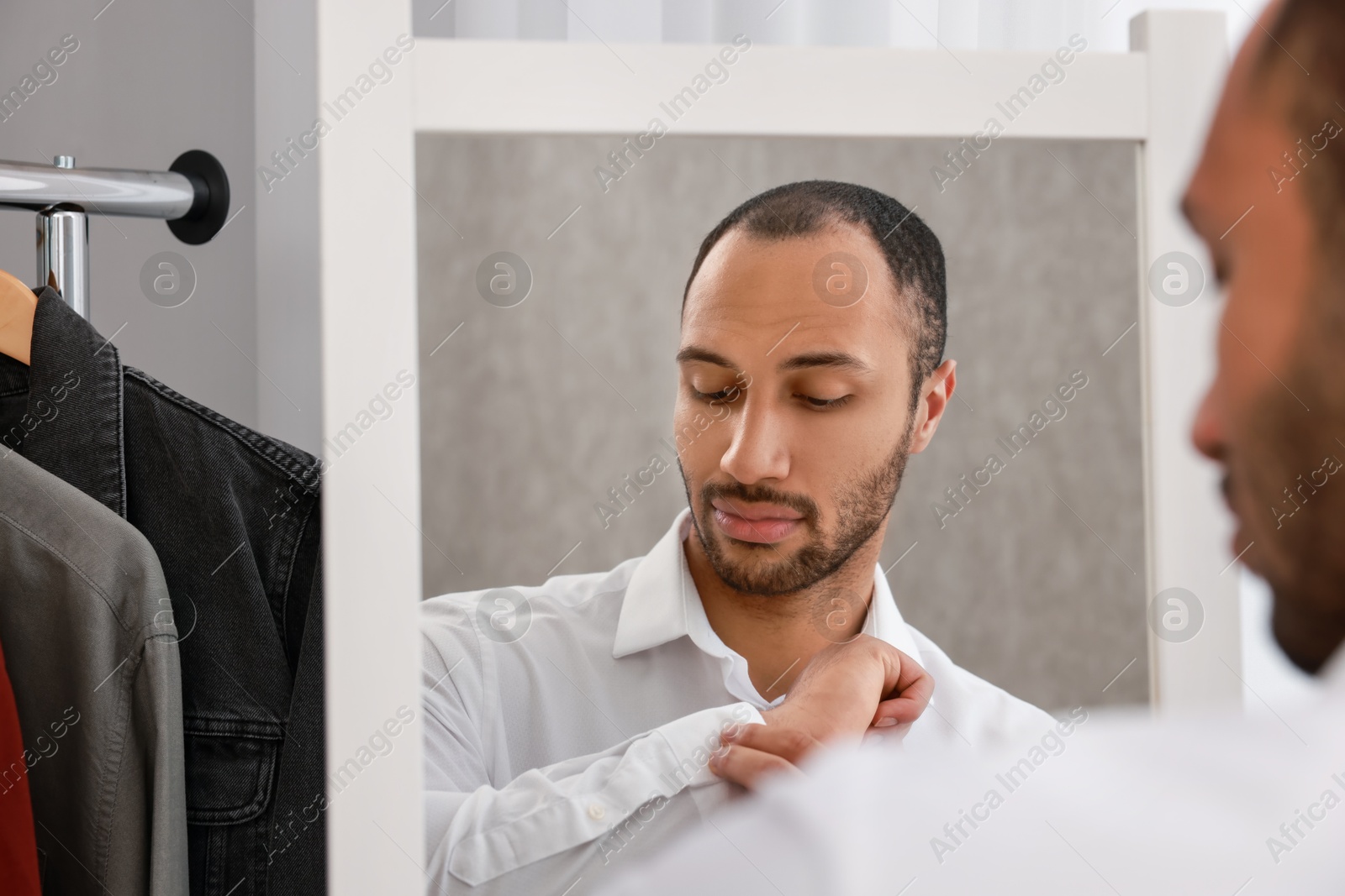 Photo of Handsome man dressing near mirror at home