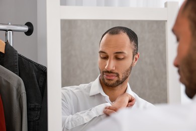 Handsome man dressing near mirror at home