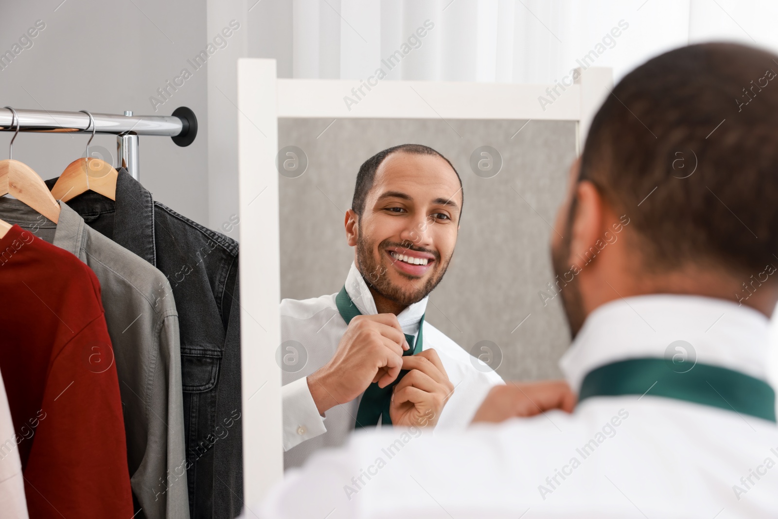 Photo of Smiling man adjusting necktie near mirror at home