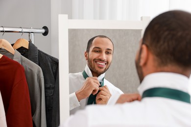 Photo of Smiling man adjusting necktie near mirror at home