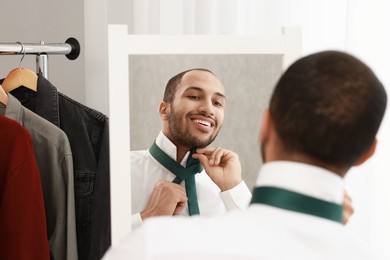 Photo of Smiling man adjusting necktie near mirror at home, back view