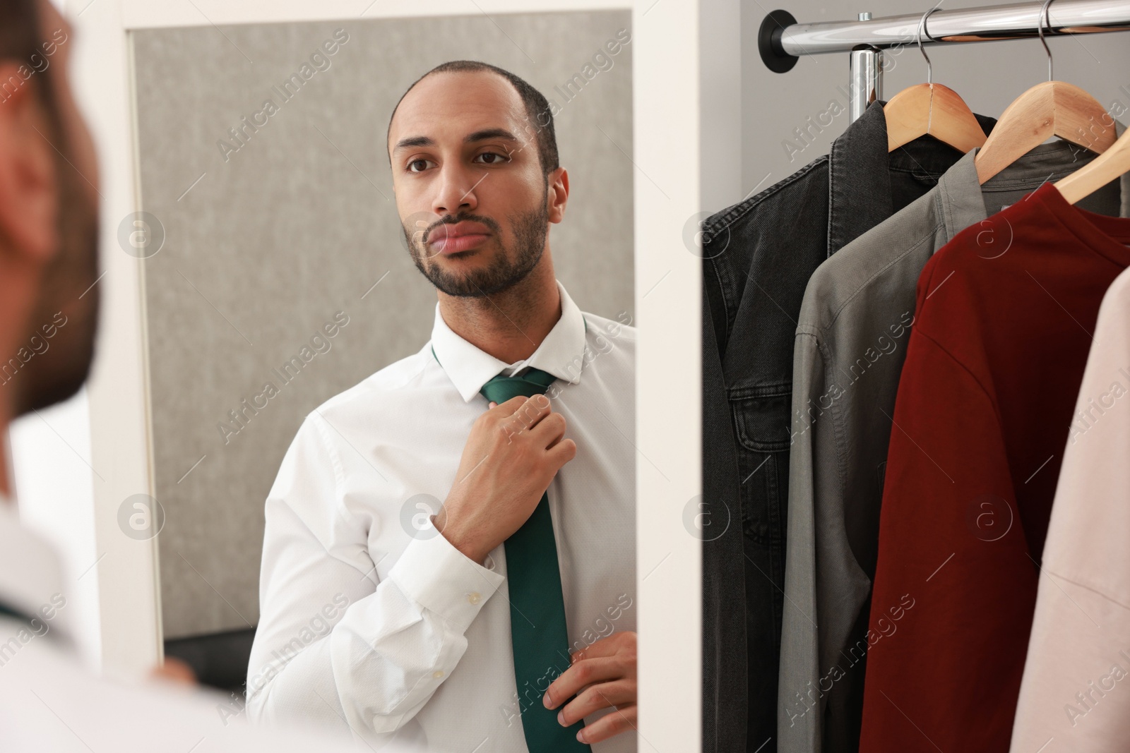 Photo of Handsome man adjusting necktie near mirror at home