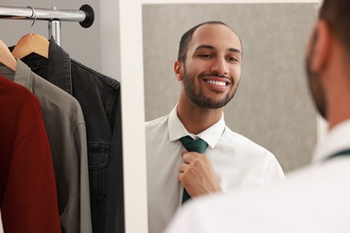 Photo of Smiling man adjusting necktie near mirror at home