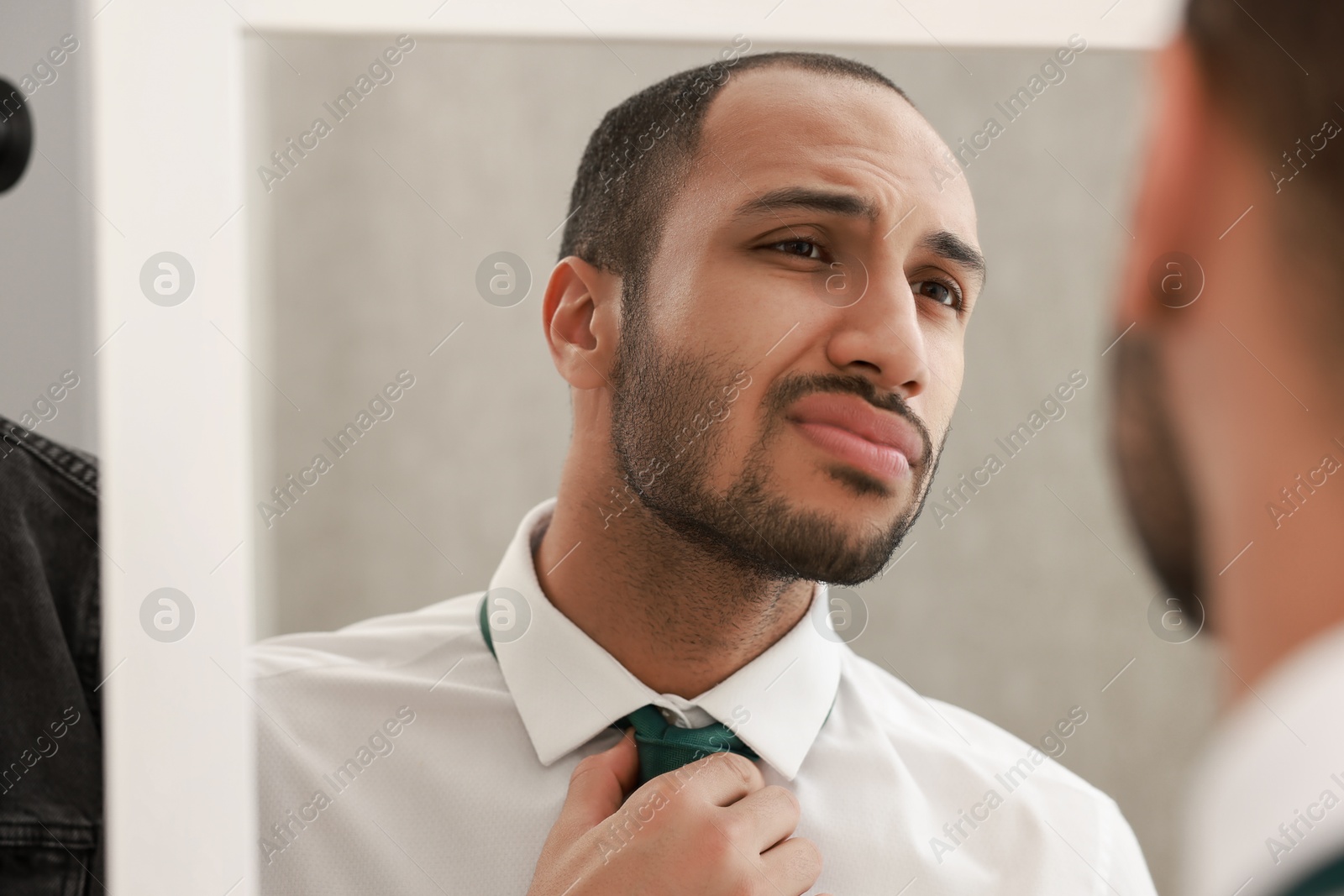 Photo of Handsome man adjusting necktie near mirror at home