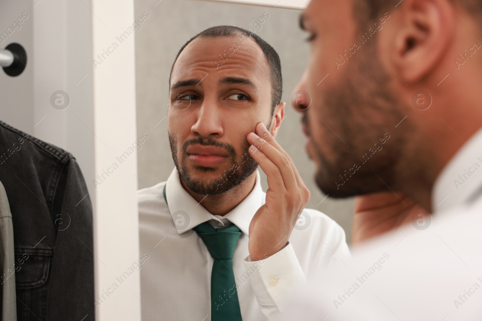 Photo of Worried man looking at mirror at home