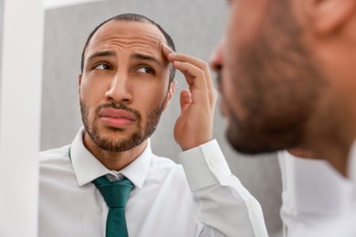 Worried man looking at mirror at home