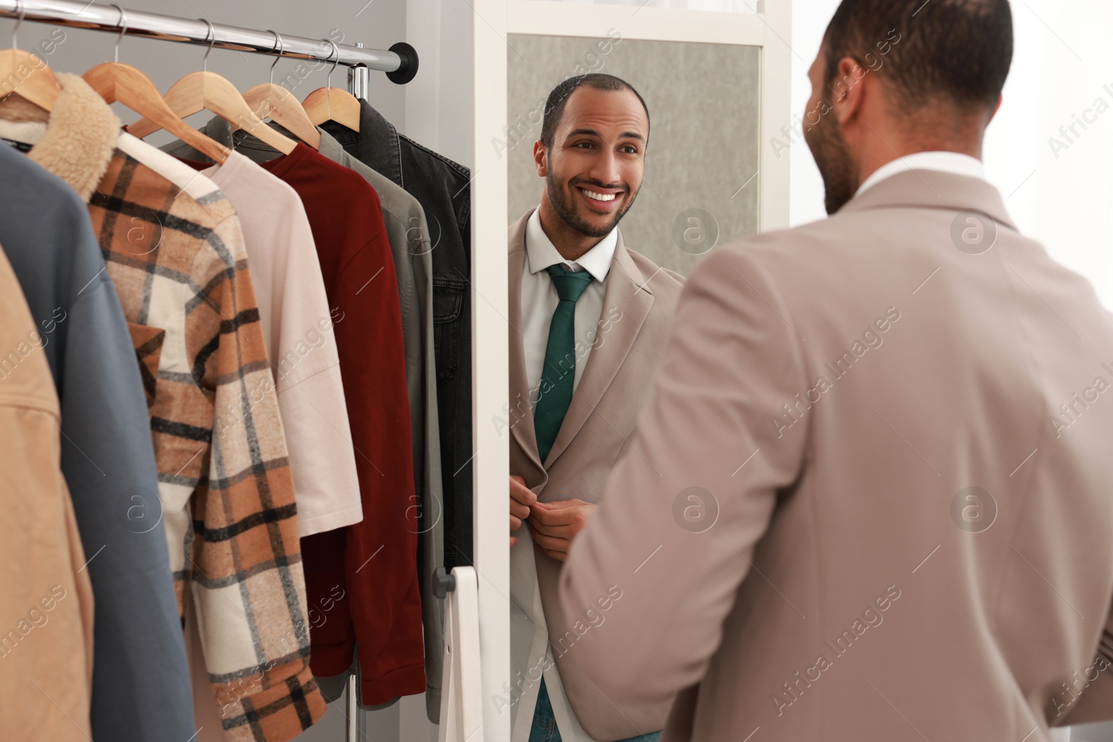 Photo of Smiling man dressing near mirror at home, back view