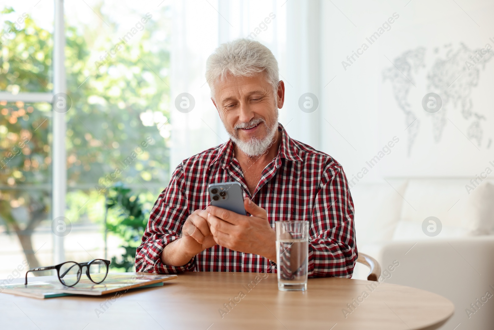 Photo of Senior man using smartphone at table indoors