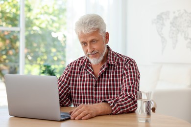 Photo of Senior man using laptop at table indoors