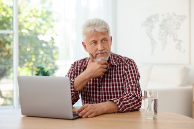 Photo of Senior man with laptop and glass of water at table indoors