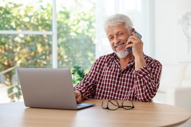 Photo of Senior man talking on phone at table indoors