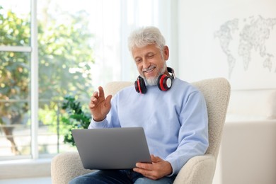 Photo of Senior man with headphones having video call via laptop at home