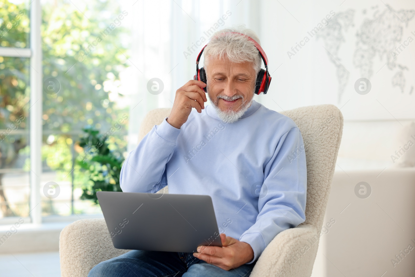 Photo of Senior man in headphones using laptop at home