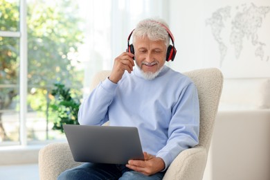 Photo of Senior man in headphones using laptop at home