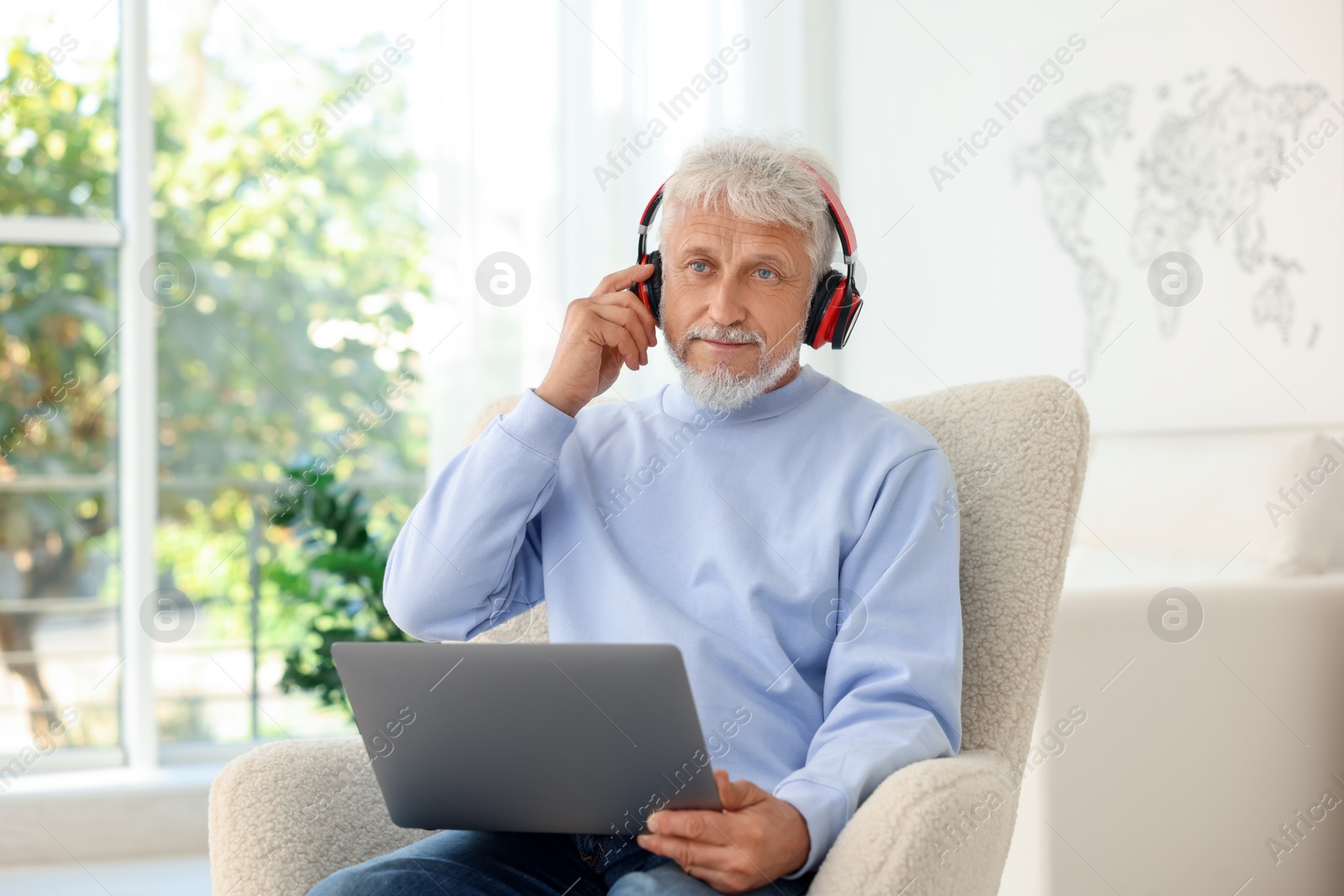 Photo of Senior man in headphones using laptop at home