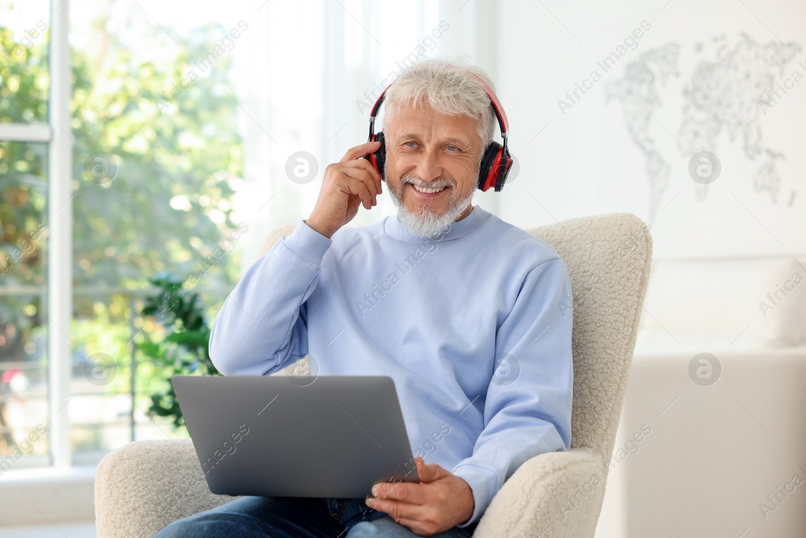 Photo of Senior man in headphones using laptop at home